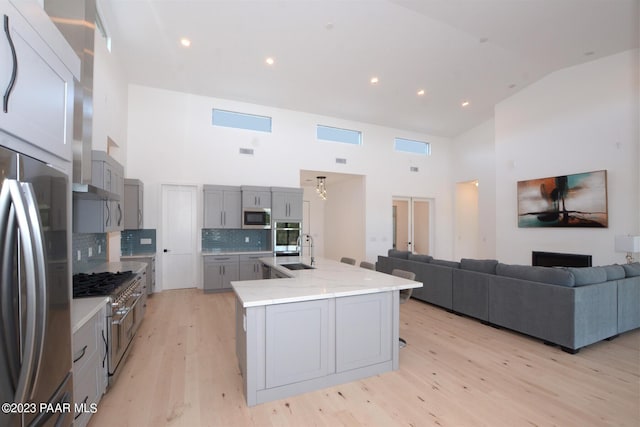 kitchen featuring decorative backsplash, appliances with stainless steel finishes, gray cabinetry, light wood-style floors, and a sink