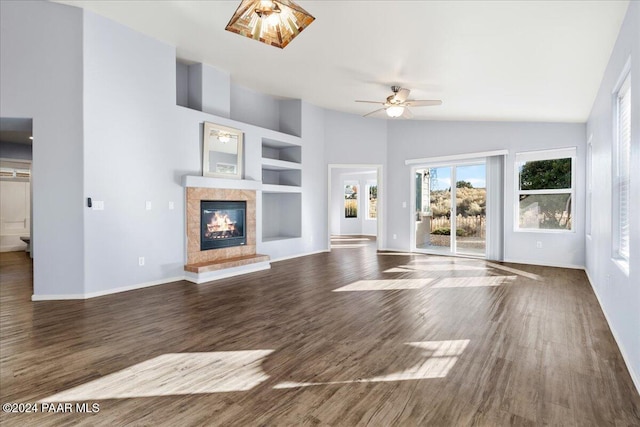 unfurnished living room with high vaulted ceiling, a tile fireplace, dark hardwood / wood-style floors, ceiling fan, and built in shelves