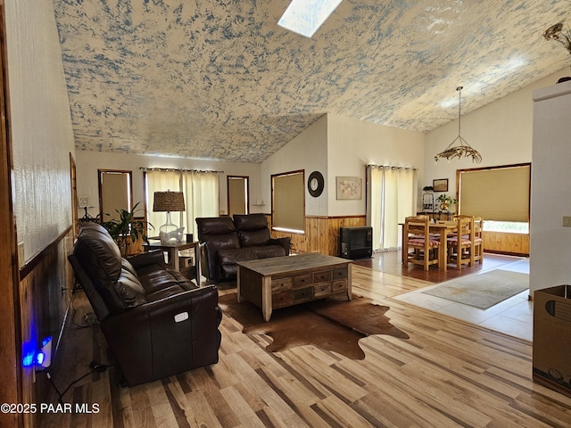 living room featuring high vaulted ceiling, light wood-type flooring, and a skylight