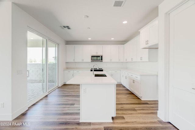 kitchen featuring white cabinets, light hardwood / wood-style floors, sink, and a kitchen island with sink