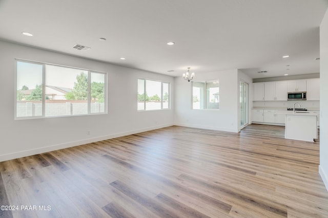 unfurnished living room with sink, light hardwood / wood-style floors, and an inviting chandelier