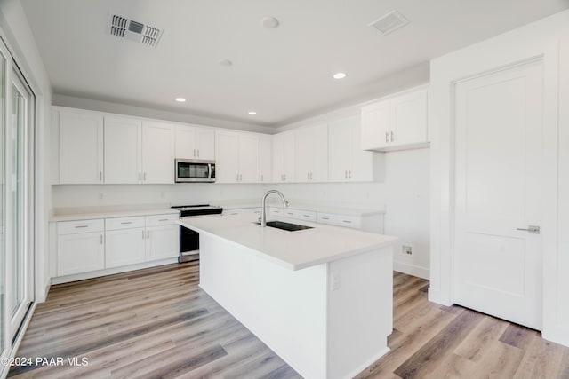 kitchen with white cabinets, sink, appliances with stainless steel finishes, and an island with sink