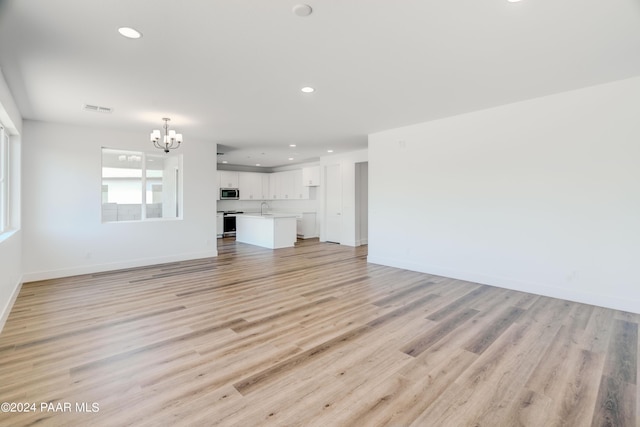 unfurnished living room featuring an inviting chandelier, sink, and light hardwood / wood-style flooring