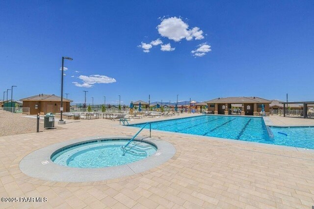 community pool with a hot tub, a patio, and fence