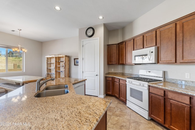 kitchen with a sink, an inviting chandelier, white appliances, pendant lighting, and light stone counters