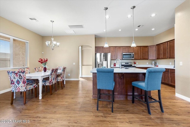 kitchen with pendant lighting, a breakfast bar area, light hardwood / wood-style flooring, a notable chandelier, and stainless steel appliances