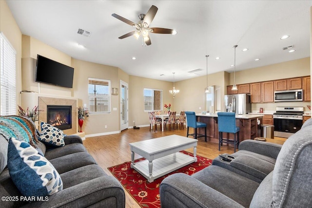 living room with ceiling fan with notable chandelier and light hardwood / wood-style floors