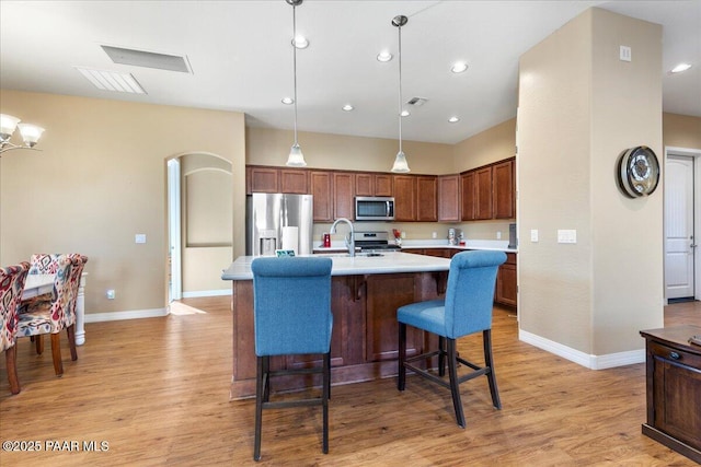 kitchen featuring appliances with stainless steel finishes, a kitchen island with sink, decorative light fixtures, light hardwood / wood-style flooring, and a breakfast bar area