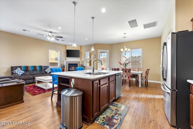 kitchen with pendant lighting, a center island with sink, ceiling fan with notable chandelier, sink, and appliances with stainless steel finishes