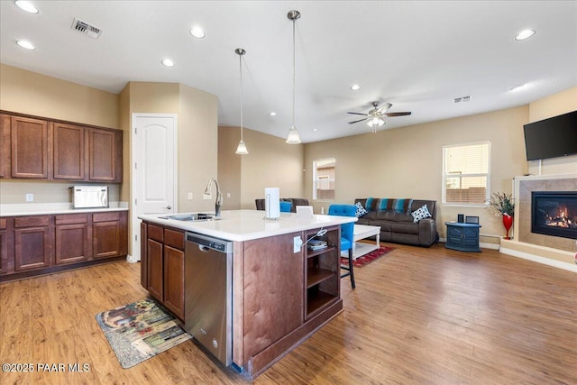 kitchen with sink, stainless steel dishwasher, decorative light fixtures, a tiled fireplace, and a center island with sink