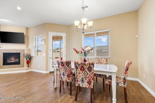 dining space with hardwood / wood-style floors, a chandelier, a wealth of natural light, and a tiled fireplace