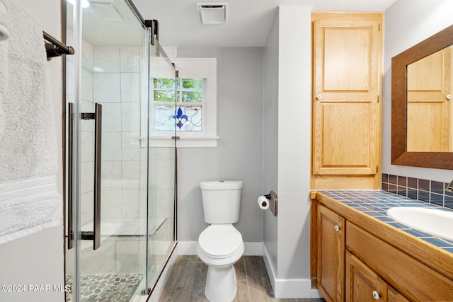 bathroom with hardwood / wood-style floors, vanity, toilet, and a shower with shower door