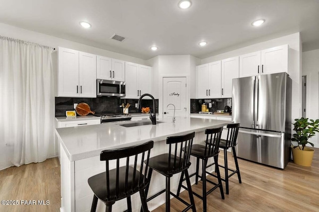 kitchen with a sink, white cabinetry, stainless steel appliances, visible vents, and light wood-style floors