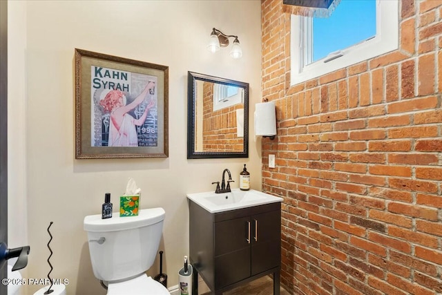 bathroom featuring vanity, toilet, and brick wall