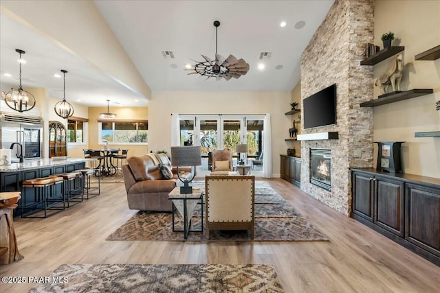 living room featuring light hardwood / wood-style flooring, a stone fireplace, plenty of natural light, and high vaulted ceiling