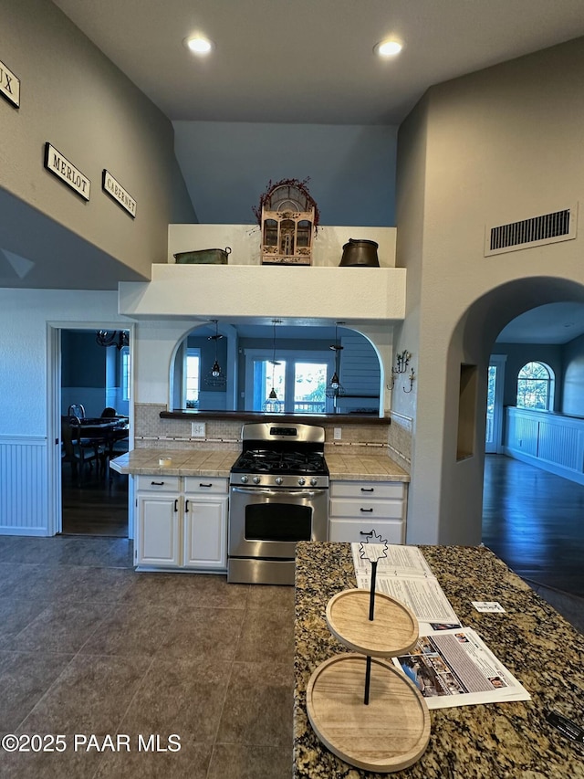 kitchen featuring stainless steel gas range, backsplash, high vaulted ceiling, white cabinets, and dark stone counters