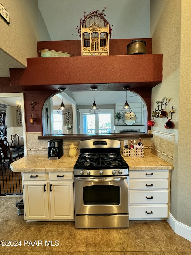 kitchen featuring pendant lighting, backsplash, gas range, and white cabinetry