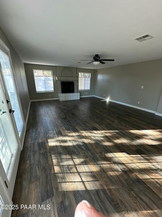 unfurnished living room with dark hardwood / wood-style flooring, a tiled fireplace, and ceiling fan