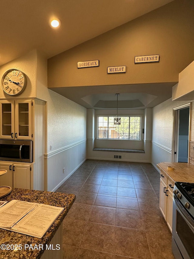 kitchen with vaulted ceiling, appliances with stainless steel finishes, pendant lighting, white cabinetry, and dark tile patterned floors