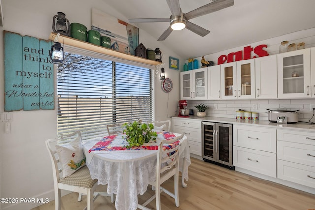 kitchen with wine cooler, light wood-style floors, white cabinets, light countertops, and vaulted ceiling