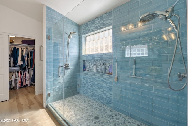 bathroom featuring a walk in closet, wood finished floors, lofted ceiling, and a stall shower