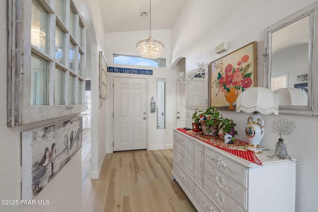 foyer with visible vents, baseboards, light wood-style flooring, a notable chandelier, and high vaulted ceiling