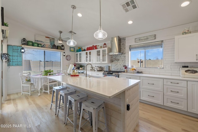 kitchen featuring visible vents, backsplash, gas range, wall chimney exhaust hood, and a sink