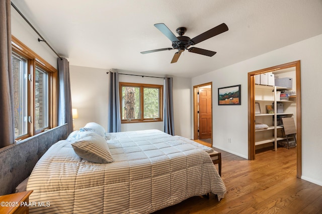 bedroom with baseboards, a walk in closet, a ceiling fan, and wood finished floors