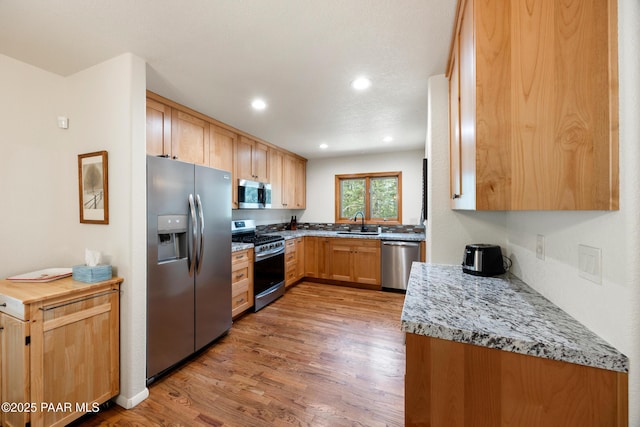 kitchen featuring a sink, stainless steel appliances, light wood-type flooring, light stone countertops, and recessed lighting