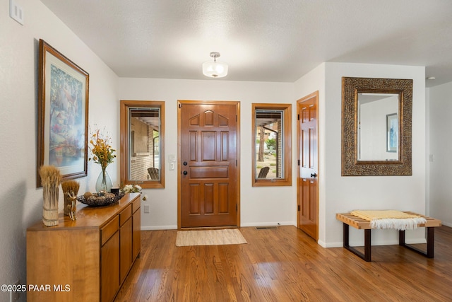foyer entrance with light wood-type flooring, visible vents, and baseboards
