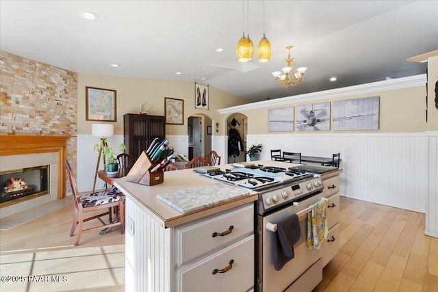 kitchen featuring gas range, white cabinetry, decorative light fixtures, a center island, and light hardwood / wood-style flooring