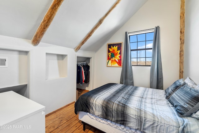 bedroom featuring a walk in closet, wood-type flooring, lofted ceiling with beams, and a closet