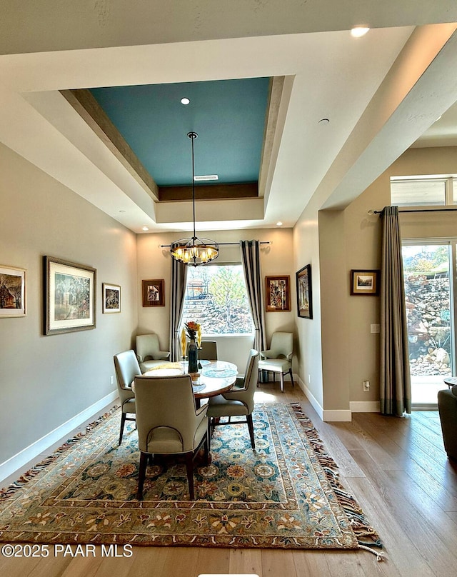dining room with a notable chandelier, baseboards, a raised ceiling, and plenty of natural light