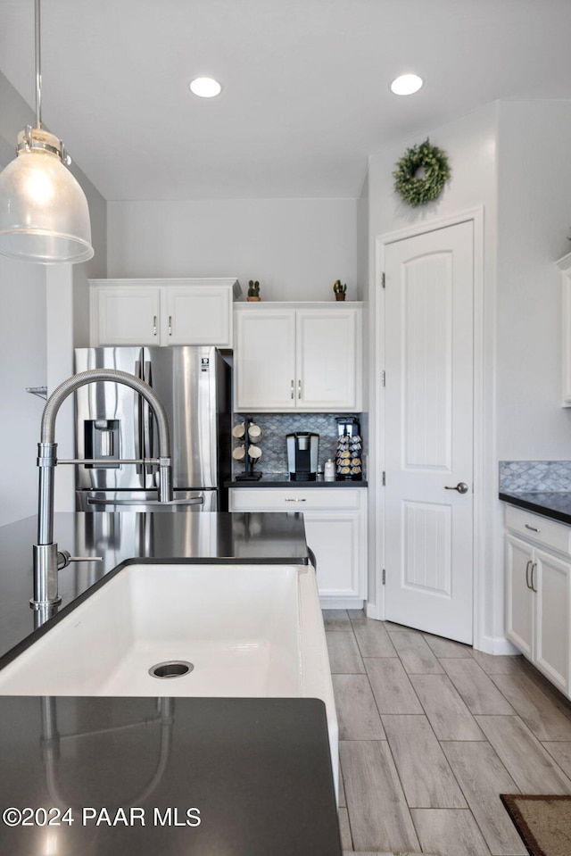 kitchen featuring hanging light fixtures, stainless steel refrigerator with ice dispenser, backsplash, light hardwood / wood-style floors, and white cabinets