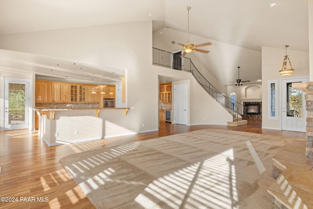 unfurnished living room with light hardwood / wood-style floors, high vaulted ceiling, plenty of natural light, and a stone fireplace