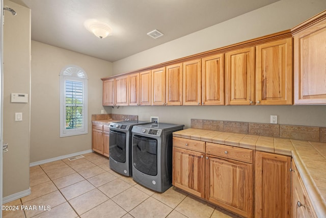 clothes washing area featuring washing machine and clothes dryer, light tile patterned floors, and cabinets