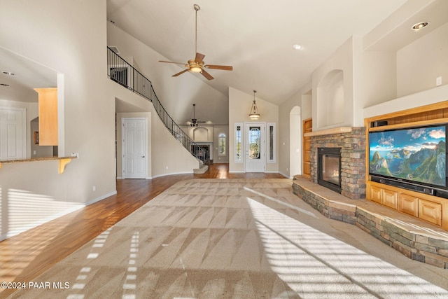 unfurnished living room with a stone fireplace, ceiling fan, high vaulted ceiling, and light hardwood / wood-style floors