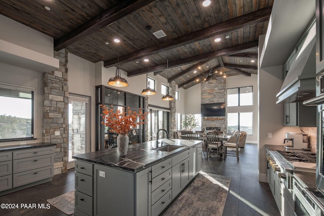 kitchen with high vaulted ceiling, a center island with sink, sink, hanging light fixtures, and beamed ceiling