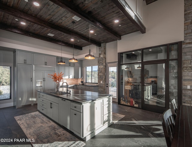 kitchen featuring sink, hanging light fixtures, beamed ceiling, an island with sink, and gray cabinets