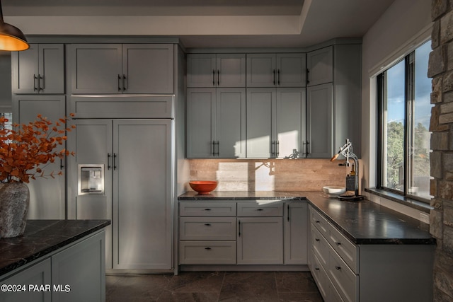 kitchen featuring gray cabinetry, paneled built in fridge, dark stone countertops, and tasteful backsplash