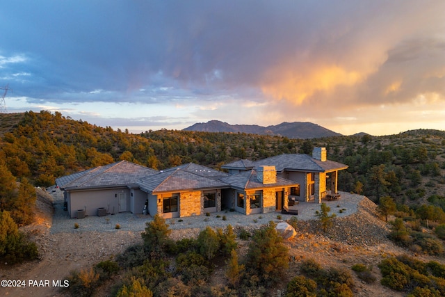 back of house at dusk featuring a forest view, a mountain view, and a chimney