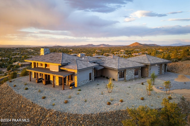 exterior space with gravel driveway, an attached garage, stucco siding, stone siding, and a mountain view