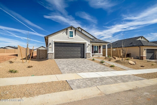 view of front facade with stucco siding, an attached garage, decorative driveway, and fence