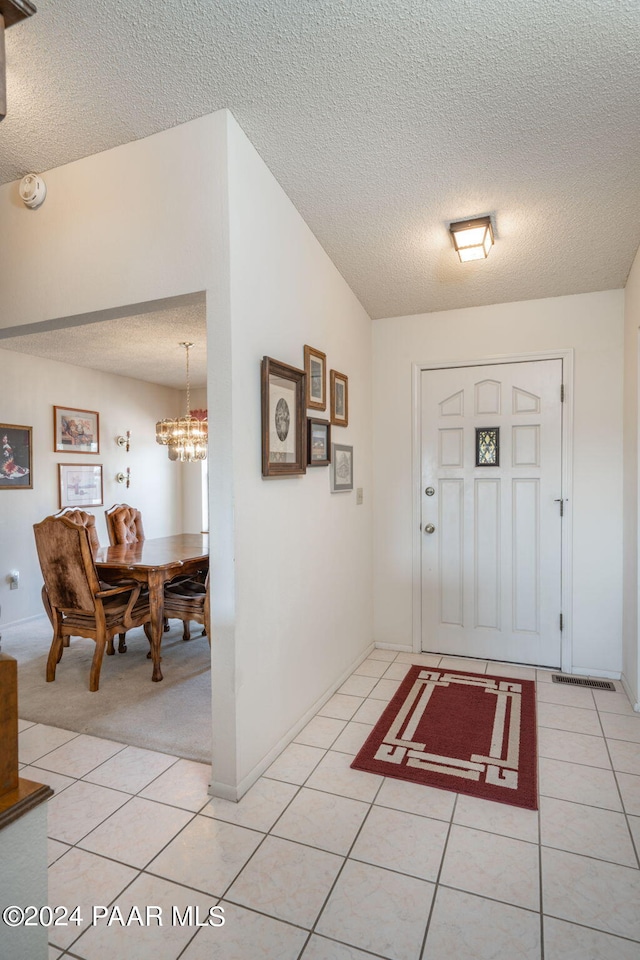 carpeted foyer featuring a chandelier, a textured ceiling, and vaulted ceiling