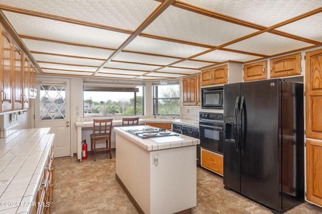 kitchen with a textured ceiling, sink, black appliances, a center island, and tile counters