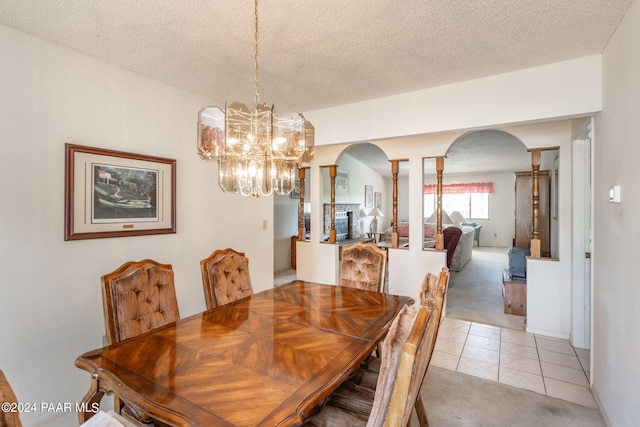 dining area featuring a chandelier, light tile patterned floors, a textured ceiling, and ornate columns