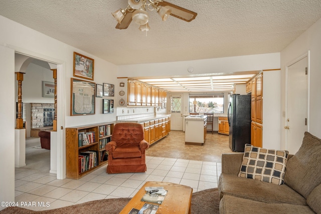 tiled living room with ceiling fan, a fireplace, and a textured ceiling