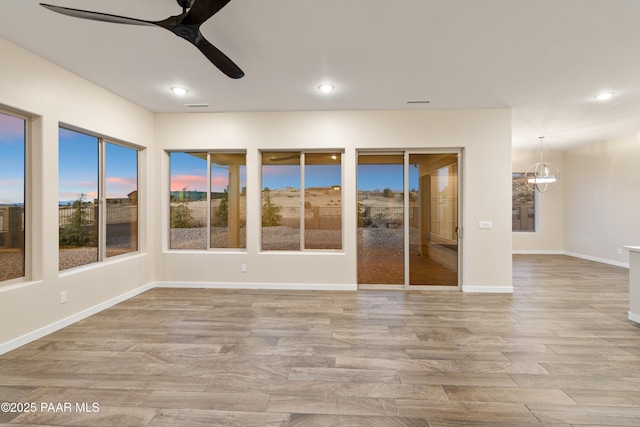 unfurnished sunroom with ceiling fan with notable chandelier and a wealth of natural light