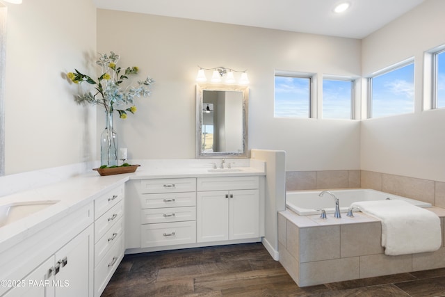 bathroom featuring wood-type flooring, a relaxing tiled tub, and vanity