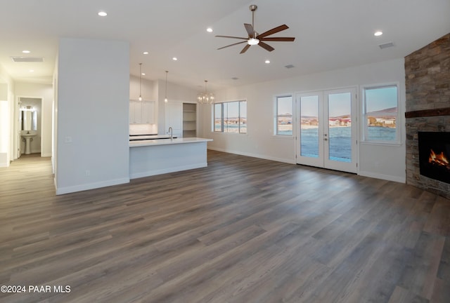 unfurnished living room featuring a stone fireplace, ceiling fan with notable chandelier, and dark hardwood / wood-style floors